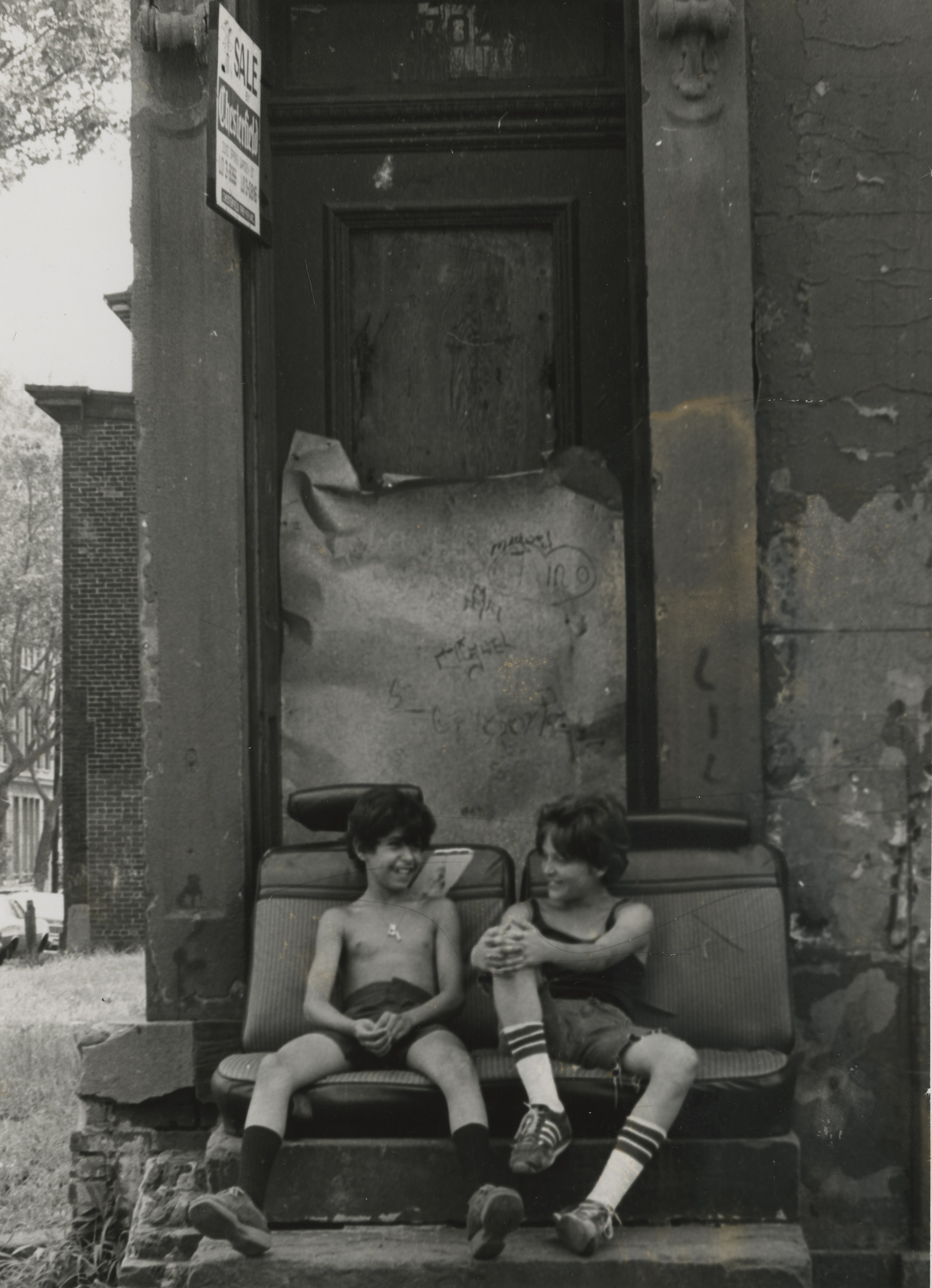 Two smiling children sit on the stoop of a house with 